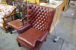 A vintage red leather wing back fireside armchair with button back and studded decoration