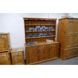 Large waxed pine dresser with open rack above three drawers and cupboards