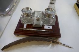 A silver and wooden desk stand with two silver topped glass square inkwells, a silver pen and wooden