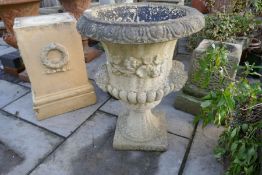 A reconstituted garden urn having figure head decoration