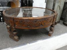 An antique style carved circular wooden table, probably Indian having glass top, 67cm