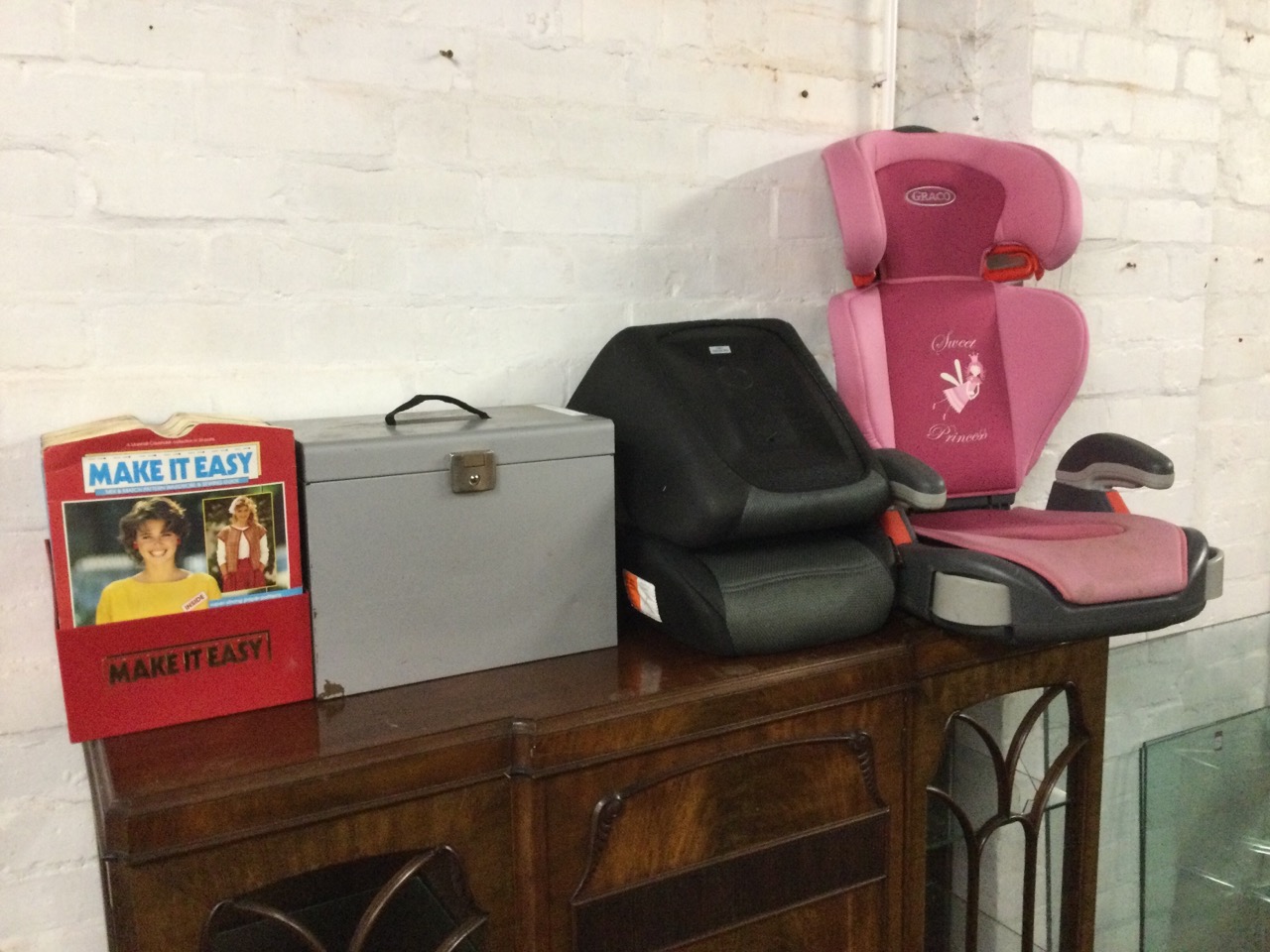 A Graco childs car seat; a pair of Halfords booster seat supports; a metal filing cabinet; and a box