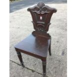 A Victorian carved oak hall chair, the tapering back with scrolled decoration around a panel, the