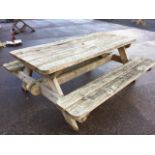 A heavy hardwood garden table & bench set, the rounded plank top with central sunshade hole above