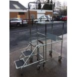 A portable work platform, the tubular trolley with three treads beneath platform framed by handrail,