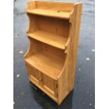 An Ercol oak whatnot cabinet with shaped sides and open shelves above panelled cupboards, with