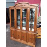 A glazed oak display cabinet, the arched crest with applied carving above four glazed doors