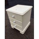 A small painted cabinet with rounded moulded top above three knobbed drawers, raised on bracket