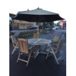 A circular teak garden table with five folding armchairs, the table on square column supports having