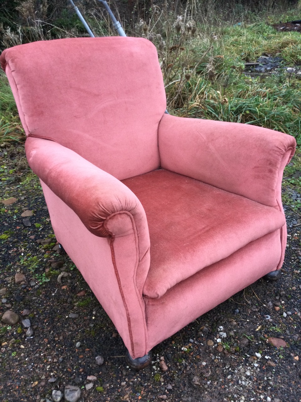 An upholstered armchair with padded back and arms above a sprung seat, raised on bun feet.