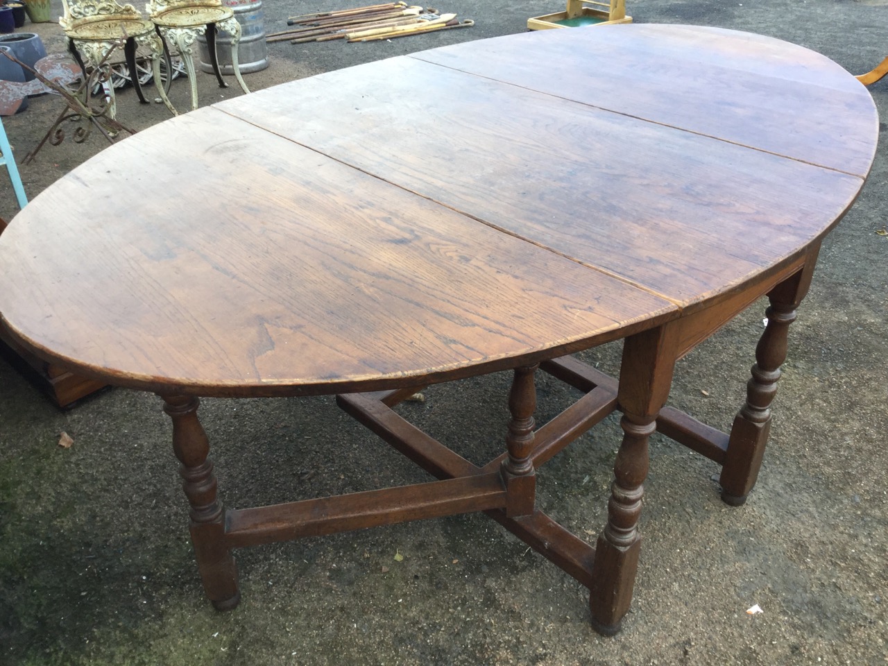 An oval oak dining table, the top with two drop leaves supported on baluster turned columns joined