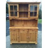 A pine dresser with moulded cornice above two glazed cupboards flanking open shelves with shaped