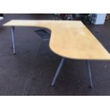 A large modern corner office desk with wide rounded work surface having shelf below, raised on