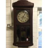 A stained 1930s wallclock with arched pediment above a glazed door and circular silvered dial,