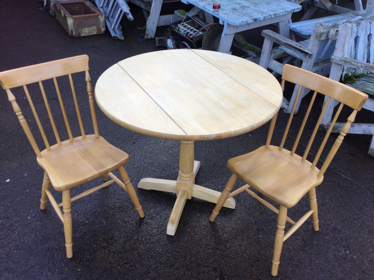 A circular hardwood table and two spindleback chairs, the table with drop leaves, the chairs in