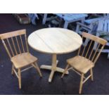 A circular hardwood table and two spindleback chairs, the table with drop leaves, the chairs in