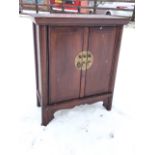 A Chinese hardwood cabinet, the panelled top with moulded cornice above two doors with central brass