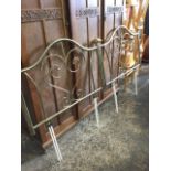 A pair of modern brass headboards with tubular arched rails framing scrolled panels, the cornerposts