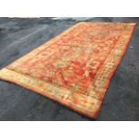 An old Turkish carpet woven with red field of floral motifs in orange, blue & cream, with a border