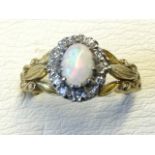 An 18ct gold opal ring with central iridescent claw-set stone framed by a border of diamonds, the