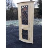A bowfronted pine corner cabinet with leaded glass doors mounted with lion ring handles, raised on
