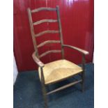 A ladderback rush-seated armchair, the back with five hipped rails above rounded arms on turned