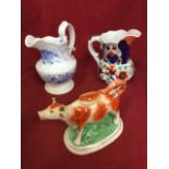 A nineteenth century cow creamer & cover with brick-red painted decoration, mounted on an oval base;