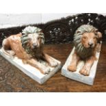 A pair of composition lions, the painted animals lying in prone positions on rectangular plinths. (