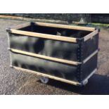 A large rectangular riveted mill bin, the box with wood slats raised on four casters. (49in x 25in x