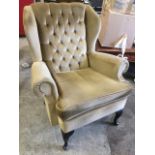 A button upholstered wing armchair with loose cushion and sprung seat, raised on cabriole legs.
