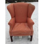 A Georgian style wing armchair, the padded back above a sprung seat with loose cushion, raised on