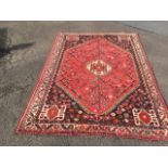 An oriental rug woven with central serrated medallion on red field with flowerheads and animal