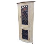 A bowfronted pine corner cabinet, the leaded glass doors mounted with lion ring handles, raised on