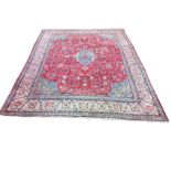 A large wool carpet, the busy red floral field framing an oval central blue medallion with