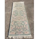 A wool runner woven in pastel floral designs on pale green ground. (98in x 33in)