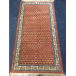 An oriental rug woven with field of paisley style motifs on red ground, within a frieze of linked