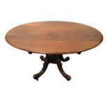 A Victorian oval tip top mahogany loo table on quadripartite baluster pedestal with scroll carved