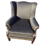 A mahogany upholstered wing armchair with sprung seat and loose cushion, the chanelled arms carved
