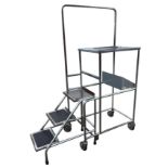 A portable work platform, the tubular trolley with three treads beneath platform framed by handrail,