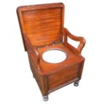 A Victorian mahogany commode the rounded hinged cover on a panelled cabinet with turned legs, the