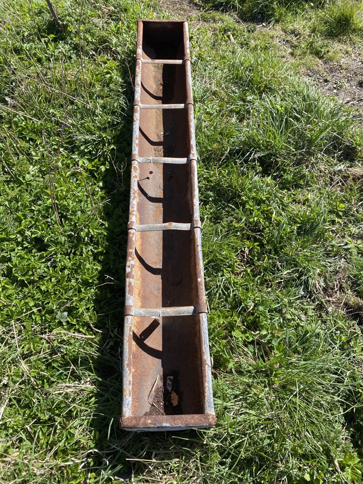 A 6ft rectangular galvanised feeding trough with tubular rim raised on bracket feet. (72in x 10in