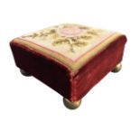 A Victorian square needlework footstool sewn with floral basket having velvet border, raised on