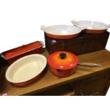 Four Le Creuset orange enamelled cast iron pieces - two oval dishes with ribbed handles, a