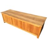 A contemporary panelled oak coffer with hinged lid, raised on square bracket feet. (61in x 19in x