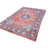 An oriental wool carpet woven with busy red field of interlaced foliage around a blue lozenge