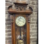 A Victorian walnut Vienna wallclock, the pediment with classical mask above an arched door framed by