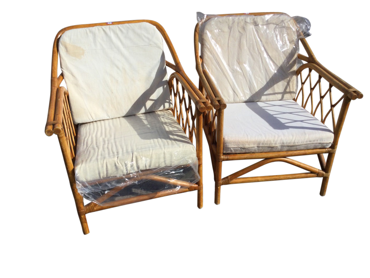 A pair of cane conservatory armchairs with loose linen upholstered cushions, the arms with stick