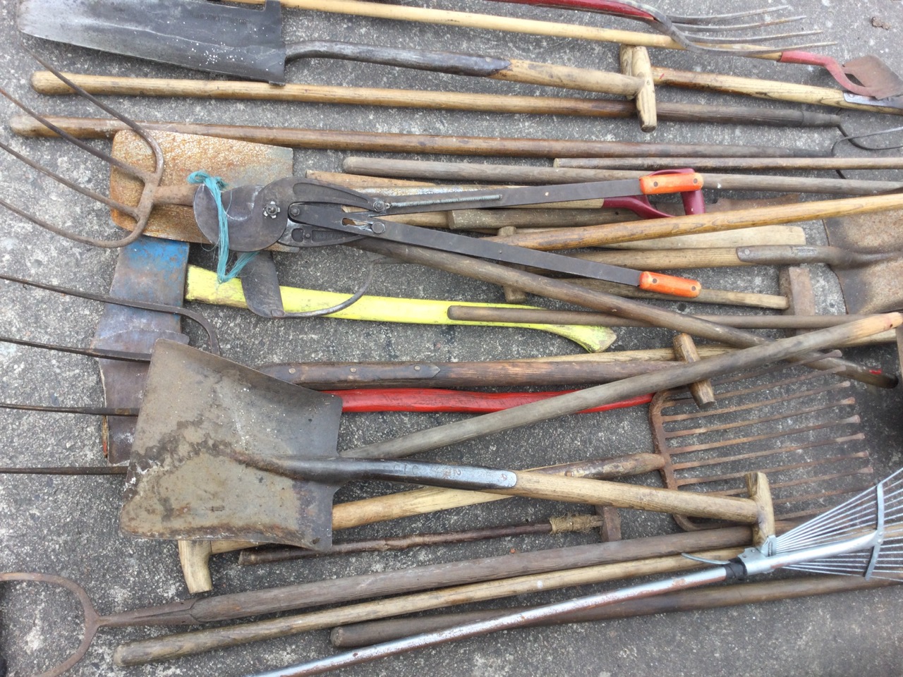 A quantity of garden tools including rakes, forks, shovels, a bolt cutter, a yard brush, hoes, pitch