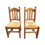 A pair of pine chairs with arched rails framing slatbacks above rush seats, raised on square