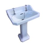 A pedestal washbasin mounted with hot & cold labelled chrome taps, having canted corners and